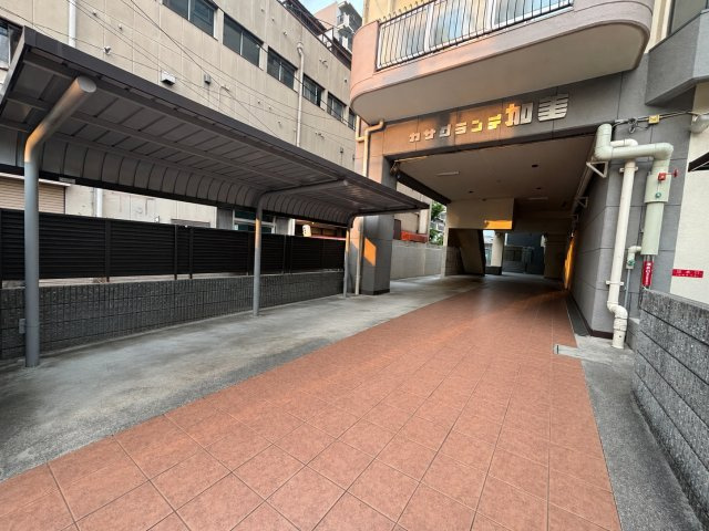 カサグランデ加美の外観|建物入口へつながる共用スペース。屋根付きのスペースが設けられており、雨の日にも利用しやすい環境です。エントランスまでの動線もゆったりと確保されています