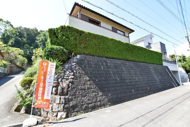 西宮市岡田山建築条件無し売土地の外観|現地には建物がありますが、解体後の更地渡しです。南東角地ならではの開放感があり、道路面より一段高くなった敷地。新しい住まいを思い描きながら、ぜひ現地をご覧ください。