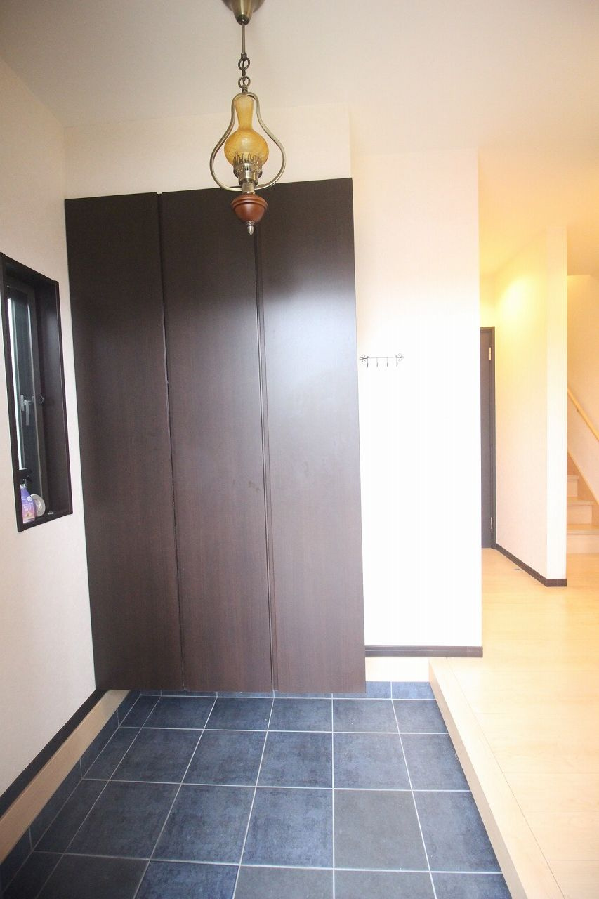 小山市出井の玄関|ダークカラーのシューズボックスと個性的な照明が目を引く玄関。収納力だけでなく、インテリアにもこだわりを感じる空間です。