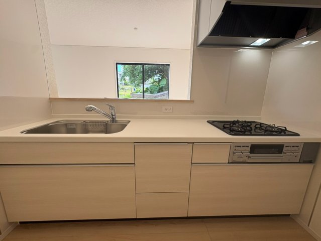 クレイドルガーデン浦添市西原　第６・２号棟のキッチン|レンジフード＆ガスコンロ３口＆浄水器付きキッチンの流し台／リビングの眺め