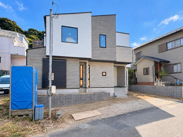 横浜市磯子区岡村１丁目の新築一戸建の前面道路含む現地写真|建物側面から撮影した現地写真。周辺は落ち着いた住宅街が広がり、前面道路や隣地との位置関係も確認できます。工事の進捗とともに住まいの全体像が少しずつ見えてきました。現地見学もお気軽にどうぞ。