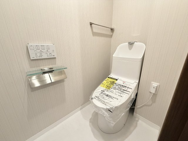 【トイレ】 | 光が丘パークタウン春の風公園街（成増店） | 上品なクロスとガラス棚付きペーパーホルダーが映える清潔なトイレ空間。壁付けリモコンの温水洗浄便座など機能面も充実し、日常の快適さを高めます。