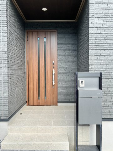 岐阜市朝霧町分譲B棟の玄関|玄関アプローチ：グレーの外壁と木目調の玄関ドアが映えます。家の“第一印象”を彩る玄関ポーチ。現地北側道路より（2026年8月）撮影 
