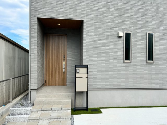 岐阜市朝霧町分譲A棟の玄関|玄関アプローチ：グレーの外壁と木目調の玄関ドアが映えます。家の“第一印象”を彩る玄関ポーチ。現地北側道路より（2026年8月）撮影 