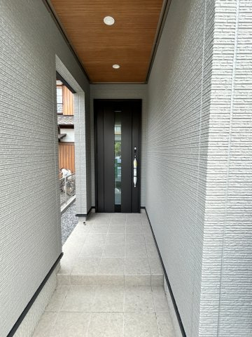 岐阜市加納南陽町分譲B棟の玄関|玄関アプローチ：ホワイト外壁に木目調の天井パネルが玄関の存在感を強調しています。家の“第一印象”を彩る玄関ポーチ。現地北側道路より（2026年8月）撮影 