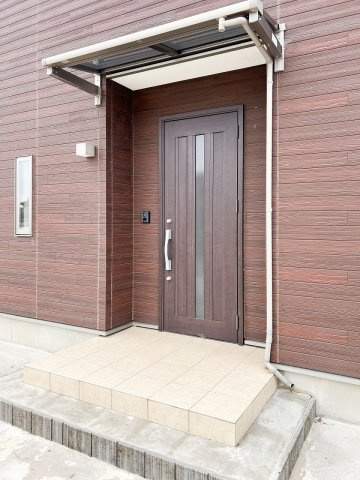 結城市山川新宿の玄関|外壁と調和する落ち着いた色合いの玄関ドア。屋根付きのポーチが、雨の日の出入りをサポートします。