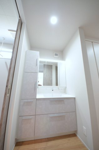 温品三丁目の洗面所|清潔感あふれるシャワー付洗面台と洗面室。鏡の裏には、歯ブラシや化粧品、ドライヤーまでスッキリ収まる大容量の収納スペースがあります。