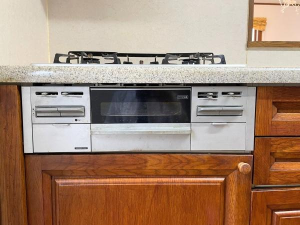 高江南1丁目　戸建てのキッチン|ガスコンロとグリルが一体になったキッチン設備です。すっきりとしたデザインでお手入れも簡単です。木目調のキャビネットが空間に温かみをプラスします。