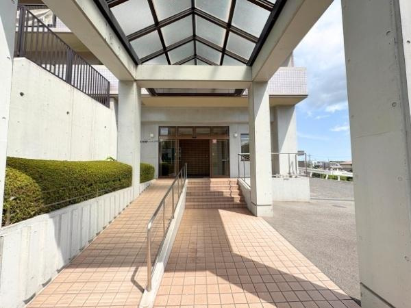東明野ハイツのエントランス|広々としたエントランスが開放感を与えます。屋根付きのアプローチで雨の日も安心です。スロープが設けられており利便性が高いです。植栽がさりげなく配置されています。