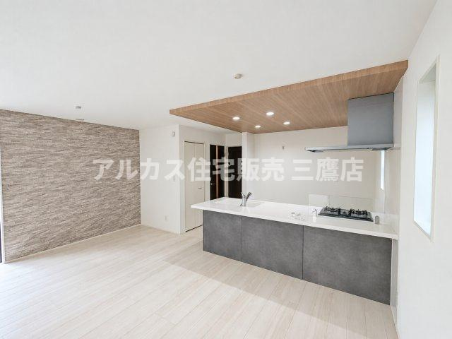 【内覧動画公開中！】三鷹市上連雀7丁目 中央線 三鷹駅 新築戸建の居間・リビング|木目調の折り下げ天井とダークグレーのキッチンが重厚感を添える、シックで洗練されたLDKです。奥のアクセントクロス壁が空間に深い奥行きを生み出しています。