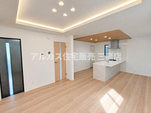 【内覧動画公開中！】三鷹市上連雀7丁目 中央線 三鷹駅 新築戸建の居間・リビング|折上天井に組み込まれた間接照明とダウンライトが、優しく空間を照らす上質なLDKです。木目調の折り下げ天井がキッチンエリアに心地よいアクセントを与えています。