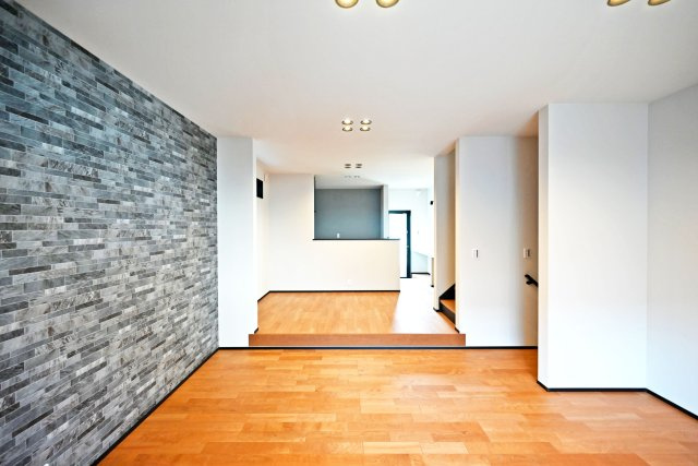 ハッピータウン豊中市本町8丁目新築一戸建て│3LDK+駐車1台可の居間・リビング|印象的なアクセントウォールが空間を引き締める、上質で洗練されたLDK。広々とした空間に木の温もりが調和し、落ち着きと品格を兼ね備えた贅沢な住空間を演出します。