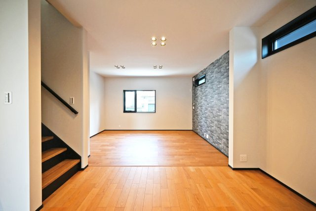ハッピータウン豊中市本町8丁目新築一戸建て│3LDK+駐車1台可の居間・リビング|1階LDKをキッチン側から正面撮影した内観写真です 。ゆとりある広さが魅力のLDK。木の温もりを感じるフローリングに重厚感のあるアクセントウォールを組み合わせ、落ち着いた上質な雰囲気に仕上げています。
