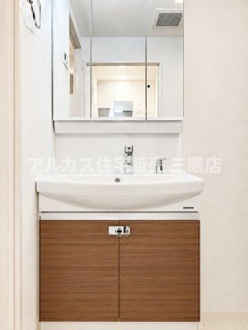 コートハウス三鷹の独立洗面台|身だしなみチェックに便利な三面鏡付きの洗面化粧台。鏡裏や下部には収納スペースを備え、木目の扉パネルがインテリアのアクセントになっています。