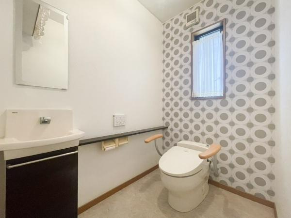 口戸　戸建てのトイレ|アクセントクロスが印象的なトイレです。手すり付きで使いやすさに配慮されています。小窓が設置されており明るい空間となっています。手洗いカウンターも備わっています。