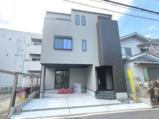 【外観】 | 中区江波西1丁目（舟入南電停）全1区画【外構込み】 | グレーを基調としたモダンな外観デザイン。1階部分には並列2台分の駐車スペース（車種による）を確保しており、雨の日の荷物運びにも便利な設計です。3階建ての構造を活かした、重厚感のある佇まいです。