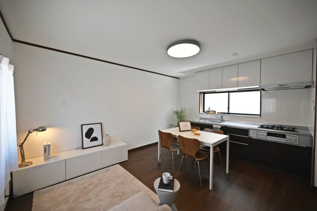 尼崎市武庫川町4丁目中古戸建│4DK+駐車1台可の居間・リビング|リフォームされたDKは、白い壁と落ち着いた色合いの床でシンプルな印象に。キッチン前にダイニングテーブルを置いても動線を確保しやすく、食事の時間からくつろぐ時間まで家族で過ごせる空間です。