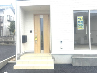 【玄関】 | 東広島市八本松飯田5丁目【JR八本松駅】（全4棟）No１ | 屋根付きのポーチを備えた清潔感のある玄関アプローチ。雨の日の出入りも安心で、木目調の玄関ドアには採光窓があり明るい空間を演出します。