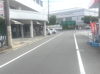 【前面道路含む現地写真】 | 南区東雲2丁目（更地）土地 | 物件から少し進んだ周辺道路の様子です。奥には「県立広島工業高等学校」が見え、平坦で整備された道が続いています。車通りや人通りの視認性も良く、毎日の通勤・通学や移動の際もスムーズに行き来できます。