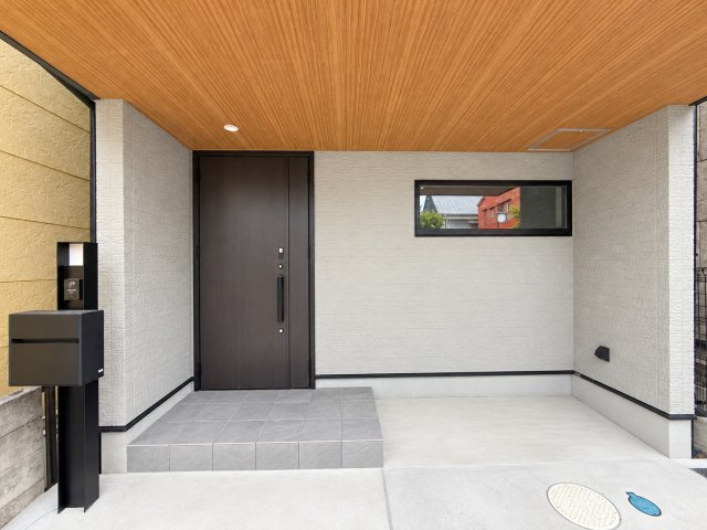 戸建 城陽市富野鷺坂山の玄関|木目調の軒天が温かみを演出する、おしゃれな玄関アプローチ♪ ブラックの玄関ドアとグレーのタイルが調和し、洗練された上品な空間が家族やゲストを迎えてくれます！