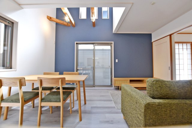 伊丹市鴻池6丁目中古戸建│4LDK+駐車1台可の居間・リビング|リビング上部の吹抜けには縦長の窓を設け、高い位置から自然光を取り込める設計。ネイビーの壁と木目の梁が目を引き、天井の高さが開放感を生み出します。