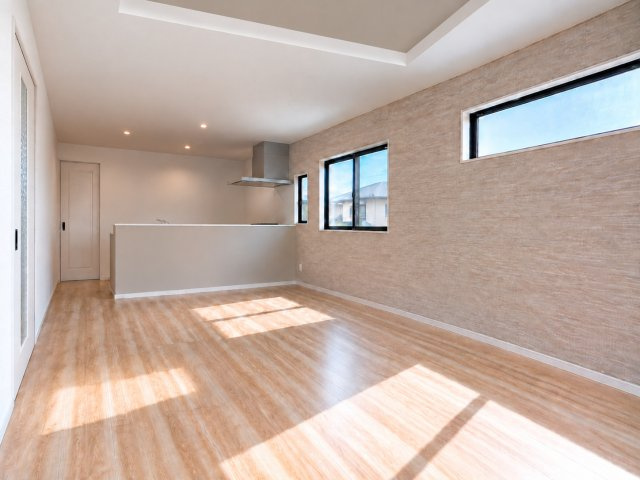 【完成予想図】 | 守谷市松ケ丘7期　新築戸建　1号棟 | 対面キッチンから家族の顔が見えるリビング。木目のアクセント壁に日差しが差し込む明るい空間です♪
※AIで作成したイメージです。床材・壁紙・色味は実際と異なる場合があります。