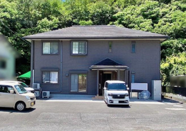 「二世帯におすすめ」高知市万々　中古一戸建ての外観|背後に緑が広がる2階建ての住まい。落ち着いた外観と、建物前のゆとりあるスペースが特徴です。
