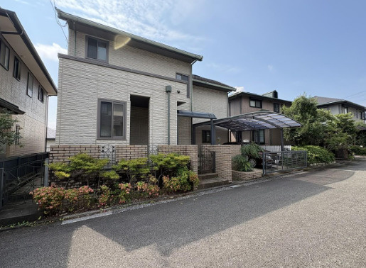 「ルーフバルコニー＆エレベーターのある4SLDK」高知市春野町南ヶ丘６丁目　中古一戸建ての前面道路含む現地写真|淡い色合いの外壁と個性的な屋根が調和する住まい。玄関まわりの植栽が彩りを添えています。