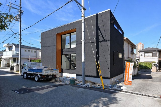 宝塚市中州2丁目新築一戸建て│3LDK+駐車1台可|ブラックを基調とした外壁に、温かな木目が美しく映える外観。直線的なフォルムが洗練された印象を与えます。大きな窓越しにはスケルトン階段が見え、外観だけでなく室内のデザインにもこだわりを感じる住まいです。