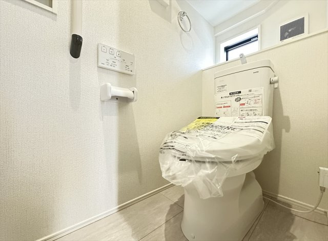 【トイレ】 | 新座市野火止3丁目　新築一戸建住宅　全61棟　(志木本店) | 手すりを備えた1階トイレ。立ち座りの動作をサポートし、幅広い世代に使いやすい設計です。壁面収納も設けられており、トイレットペーパーなどの日用品をすっきり整理できます。