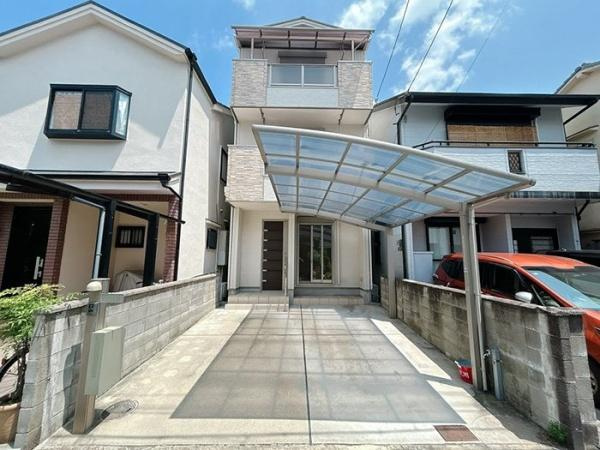 枚方市 楠葉中町　中古 一戸建ての外観|青空に映えるスタイリッシュな3階建て住宅。大きなカーポートが愛車を雨や日差しから守ります。ゆとりある駐車スペースも魅力。ぜひ現地で住まいの魅力をご体感ください。