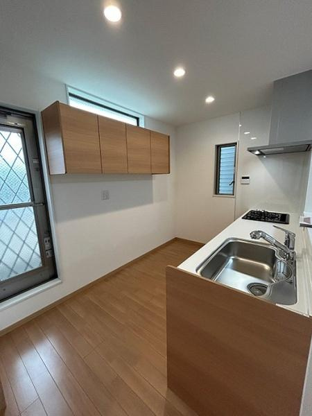 枚方市 楠葉中町　中古 一戸建てのキッチン|ッチン背面には木目調の吊戸棚を備え、食器や調理用品をすっきり収納。足元にもゆとりがあり、家事動線を確保しやすい設計です。窓から自然光が差し込む、明るく清潔感のあるキッチン空間です。