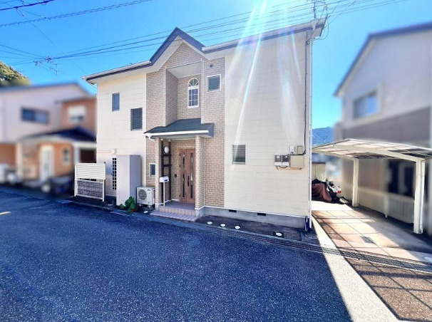 高知市南河ノ瀬町の中古一戸建の前面道路含む現地写真|左右対称の窓と玄関が印象的な外観。建物の配置や駐車スペースも、ぜひ現地でご確認ください。