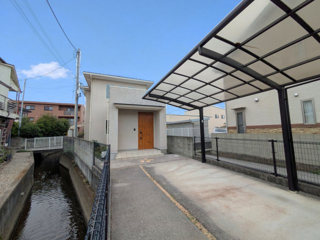北土居5丁目戸建ての外観|落ち着いた色合いの外観に木目調の玄関扉が映える戸建て。屋根付きのカーポートを備えています。