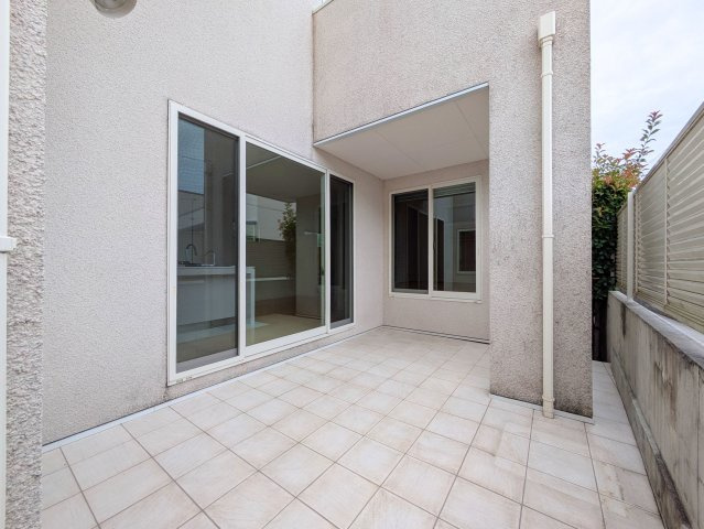北土居5丁目戸建てのバルコニー|室内の掃き出し窓につながるタイルテラス。建物の壁と柱に囲まれ、一部に軒が掛かっています。