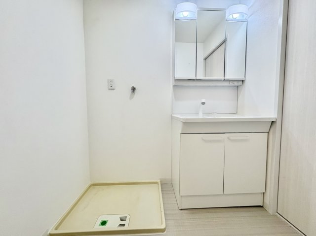 荒神山マンションの独立洗面台|身支度に便利な三面鏡付き洗面台。鏡裏や足元に豊富な収納を完備し小物をすっきり片付けられます。すぐ横に洗濯機置き場が並ぶスムーズな家事動線も魅力で、毎日の生活ワークを快適にサポートする洗面室です。