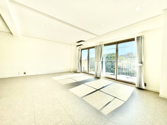 荒神山マンションの居間・リビング|大きな窓から心地よい陽光がたっぷりと差し込む、広々とした約18帖の広大リビング。ダウンライトがスタイリッシュな空間を演出し、家族が集まってもゆったりと開放的に過ごせる、住まいの主役にふさわしい一室です