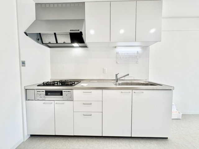 荒神山マンションのキッチン|白を基調とした清潔感あふれるシステムキッチン。壁面にすっきりと収まる配置のため、リビングスペースを無駄なく広く使えます。上下に豊富な収納スペースを備え、調理器具や食器もすっきりと綺麗に片付きます
