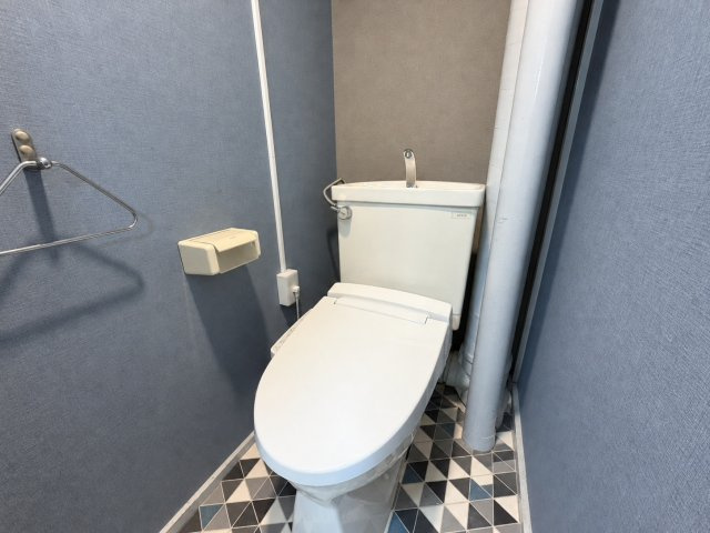 東部コーポ1号棟のトイレ|グレー系の壁紙に、幾何学柄の床を合わせたトイレです。白い便器とのコントラストがあり、コンパクトな空間