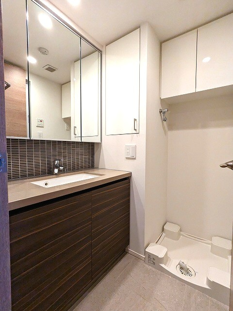 ザ・パークハビオ根岸三丁目の洗面所|三面鏡付トイレと独立した洗面台です。
洗濯機置場のお手入れ楽な足高の防水パンに排水口を手前中央に配置