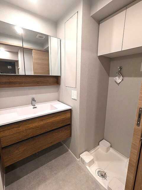 ミリアレジデンス蔵前の洗面所|トイレと独立した2面鏡付洗面台、洗面台下にヘルスメーターストックあります、洗濯機置場はお手入れし易い様に排水口を手前中央に配置し、足高の防水パンです