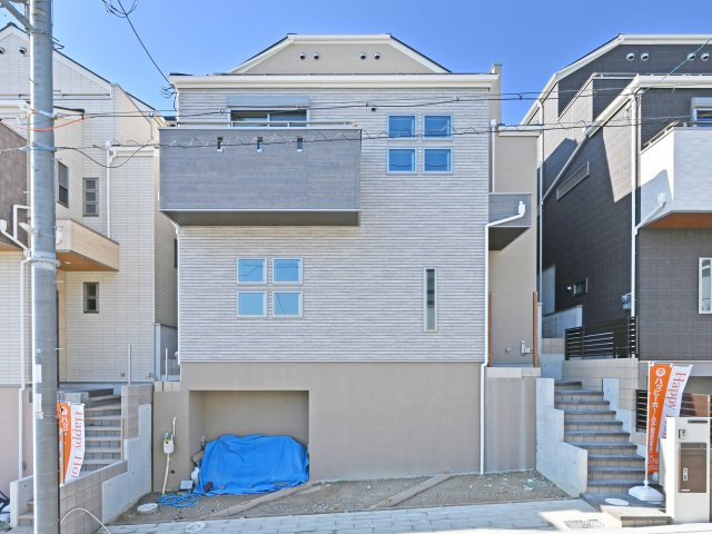 五月ケ丘新築一戸建て｜4LDK+駐車2台可の外観|B号棟の正面外観写真です。傾斜地に建つ分譲地で、基礎を高く設けています。基礎部分を一部掘ることで普通車を全棟2台駐車できるように設計しています。アプローチ幅も大きく、季節毎の演出まで楽しめる住宅です。