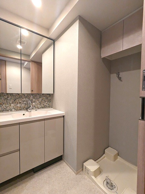 SEASON FLATS Shinokachimachiの洗面所|トイレと独立した洗面室、ハンドシャワー付き、2面鏡付き洗面室の下にヘルスメーターストックスペース付き、洗濯機置場のお手入れし易い様に排水溝を手前中央に配置し、足高の防水パンです