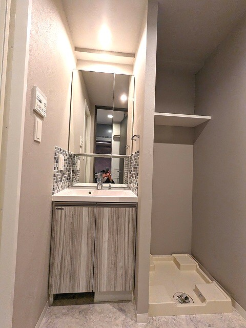 GRAND CONCIERGE浅草橋の洗面所|洗面台の下にヘルスメーターストックスペースあります。洗濯機置場はお手入れしやすい様に足高の防水パンで、排水溝を手前の中央に配置しています