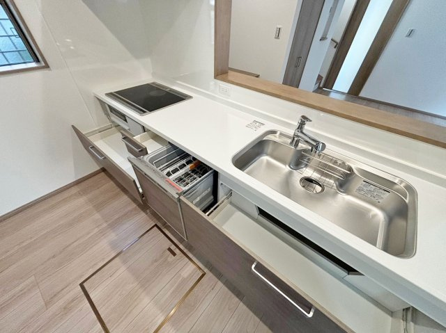 サニーサイド寺本1丁目新築戸建│3LDK+駐車駐輪可（車種制限有）のキッチン|ワークトップ下いっぱいに収納庫を設け、コンロ下にはスパイス収納も配置している2550mm幅のユニットを採用。食洗器と浄水水栓も標準仕様です。IHコンロでお掃除の際もラクラクです。