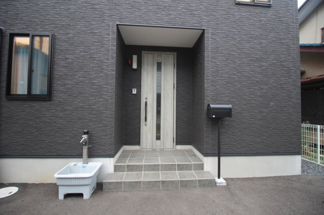 下野市駅東4丁目の玄関|スタイリッシュな玄関ドアが映えるエントランス。屋根付きポーチで雨の日の出入りも安心です。外水栓やポストも備わっており、使い勝手の良い玄関まわりになっています。