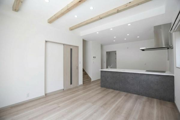 AG-HOUSE　上田町　B棟の居間・リビング|リビングに木目調のフローリングが広がり天井の梁が空間にアクセントを加えています。キッチンカウンターが一体化されていて開放的な雰囲気があります。室内は白を基調とした落ち着いたデザインになっています。