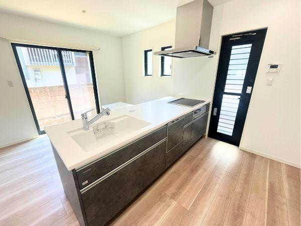 AG-HOUSE　光吉　A棟のキッチン|白とダークカラーのコントラストが美しい対面式キッチン。開放感があり、家族と会話を楽しみながら料理ができる設計。背面ドアや2面採光で換気・採光も良好、快適な家事動線を実現しています♪