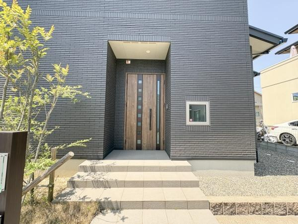 京が丘南4丁目　中古の玄関|重厚感のある玄関扉が建物全体の雰囲気に調和しています。ステップやアプローチ部分も広々としており開放感を感じられます。外壁のシックなカラーと木目の扉がモダンな印象を与えます。