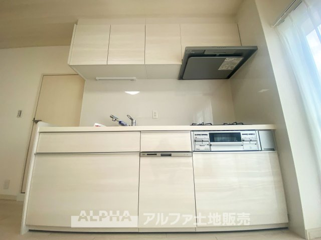 立川羽衣町住宅2号棟のキッチン|白を基調にしたシンプルで清潔感あふれるキッチン。3口ガスコンロと食器洗い乾燥機が完備され、効率よく料理が進められます。収納も充実しており、整理整頓がしやすいのが特徴です。